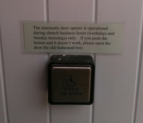 A door opener with a sign over it, sliver button with wheelchair person on it